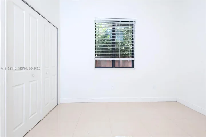 Neutral-toned tile flooring, white paneled closet doors, and a window with horizontal blinds