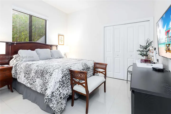 Bedroom featuring large-format tile flooring, multi-panel window with horizontal blinds, and bi-fold closet doors