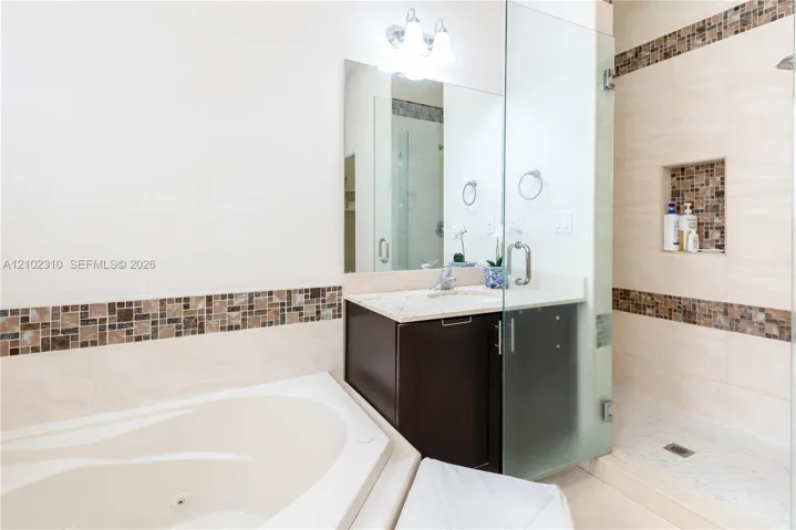 Bathroom featuring a soaking tub, glass-enclosed shower with a tiled recessed niche, vanity with a stone countertop, and decorative mosaic tile accents