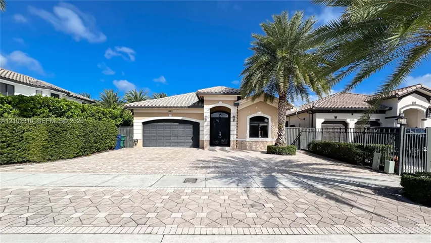 Single-story residence featuring a tile roof, arched entryway, paved driveway, and mature palm tree