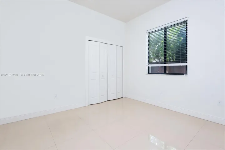Neutral-toned tile flooring, white-panel bifold closet doors, and a single-pane window with horizontal blinds
