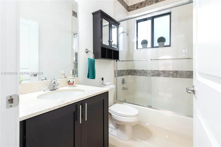 Dark-finish cabinetry vanity with stone-surfaced countertop, integrated sink, mirrored medicine cabinet, and shower-tub combination featuring tiled decorative accents and sliding glass doors