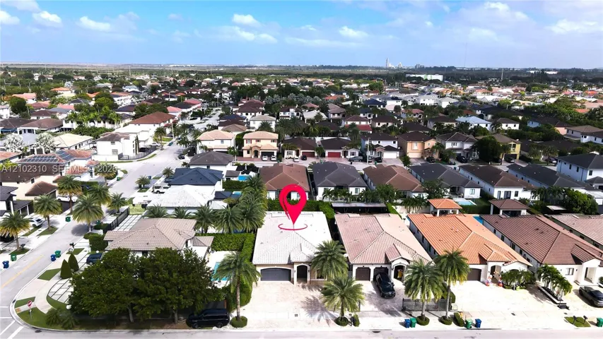 Aerial perspective of single-story residence featuring a tile roof, paved driveway, two-car garage, and mature landscaping