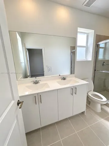 Dual-sink vanity with white cabinetry, light-toned countertop, large wall-mounted mirror, and tile flooring