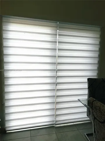 Dual-pane sliding glass door featuring adjustable light-filtering zebra roller shades and ceramic tile flooring