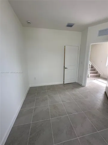 Neutral interior space featuring large-format ceramic tile flooring, solid-core panel interior door, and high ceilings