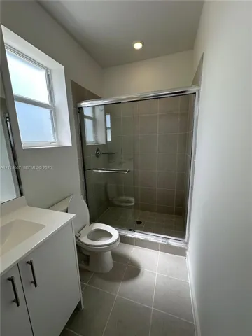 Full-height glass shower enclosure with neutral-toned tiled surround, vanity with integrated basin, polished metal hardware, and ceramic tile flooring