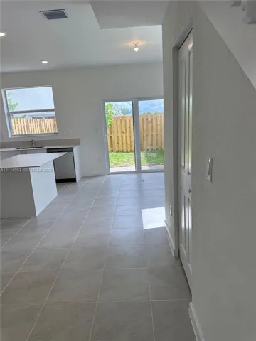 Ceramic tile flooring, white kitchen cabinetry with a central island, recessed ceiling lighting, and sliding glass doors providing access to the backyard