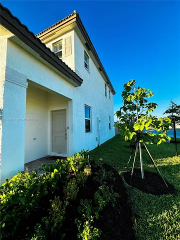 Two-story stucco exterior with a covered entryway, paneled front door, and manicured landscaping featuring dark mulch beds and a young specimen tree