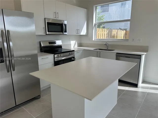 Kitchen featuring white flat-panel cabinetry, a central island with a solid surface countertop, stainless steel appliances, and large-format tile flooring