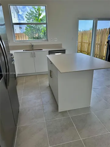 Kitchen featuring a central island, solid-surface countertops, white cabinetry with metallic hardware, stainless steel appliance, and ceramic tile flooring