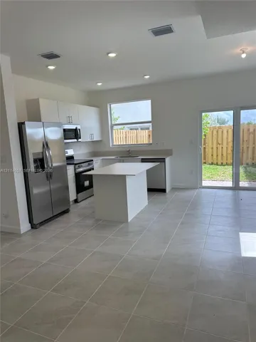 Kitchen featuring white flat-panel cabinetry, stainless steel appliances, a center island with solid-surface countertop, tile flooring, and sliding glass doors