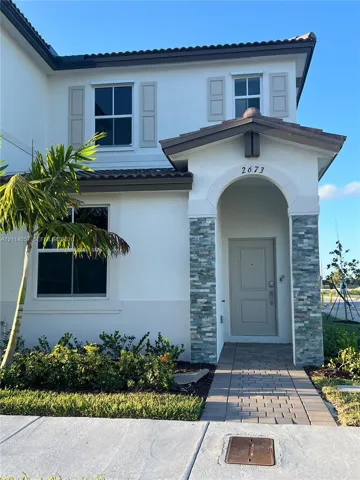 Two-story stucco exterior featuring a stone-veneer entry arch, arched recessed doorway, paneled shutters, and paver walkway