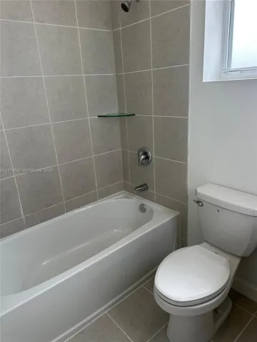 Full bathroom featuring a white porcelain tub, chrome shower fixtures, glass corner shelf, and neutral-tone tile surround