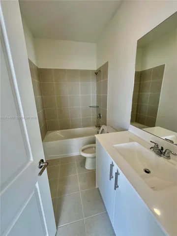 Bathroom featuring a white vanity cabinet with an integrated rectangular sink, a large wall-mounted mirror, and ceramic tile flooring