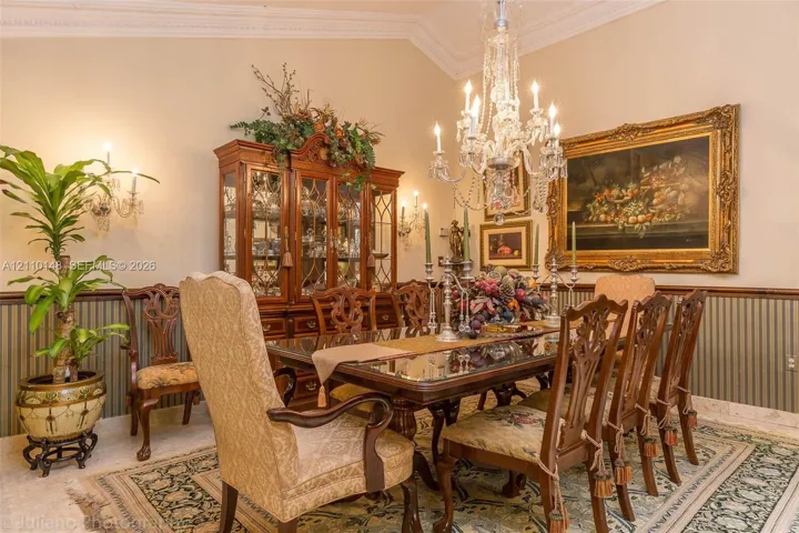 Formal dining space featuring intricate crown molding, decorative chair rail, wall-mounted light sconces, and a multifaceted crystal chandelier