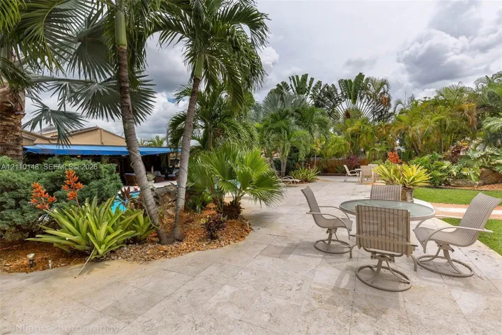 Expansive stone-paved patio featuring established palm trees, landscaped garden beds, and manicured lawn areas