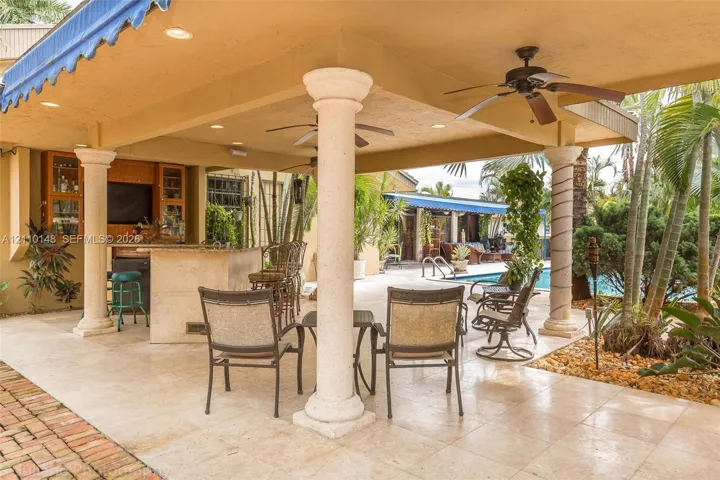Covered outdoor patio featuring stone flooring, integrated bar with cabinetry, structural decorative columns, recessed lighting, and dual ceiling fans