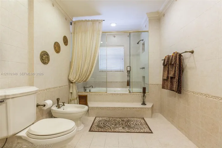 Full-tiled bathroom featuring a soaking tub, glass-enclosed shower, bidet, and crown molding