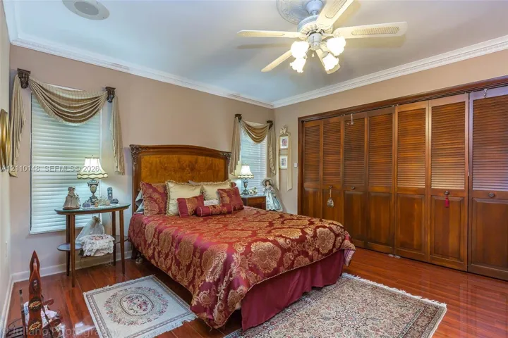 Wood-finish flooring, full-length built-in wooden louvered-door closets, crown molding, and a central ceiling fan with an ornate medallion