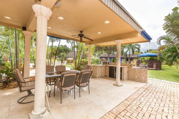 Covered outdoor patio featuring recessed lighting, a stone-finished built-in kitchen, decorative columns, and brick paver flooring