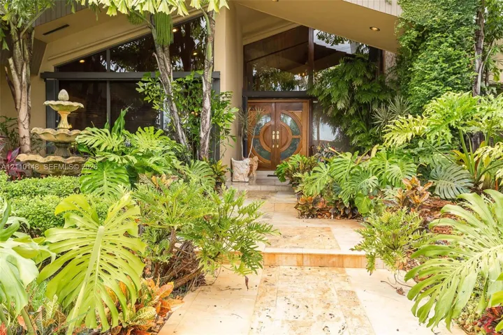 Architectural entryway featuring vaulted rooflines, floor-to-ceiling multi-pane windows, double wood doors with circular glass inlays, and a multi-tiered stone fountain