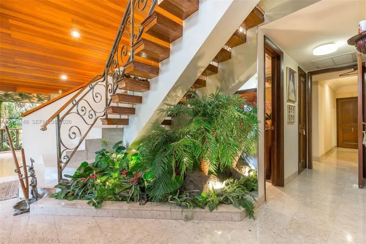 Open-tread staircase featuring wood-finish steps and custom metal scrollwork railing, wood-paneled ceiling, integrated interior planter with stone elements, and polished stone flooring