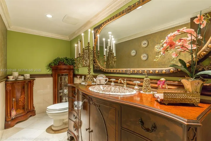 Custom dark-stained wood cabinetry vanity with patterned basin, expansive wall-mounted mirror with decorative frame, crown molding, and polished stone tile flooring