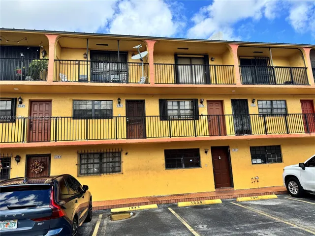 Multi-story stucco exterior featuring second-level covered balconies with black metal railings and designated paved parking spaces