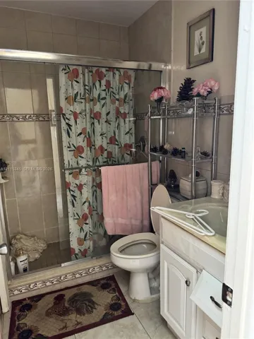 Shower enclosure with sliding glass doors, ceramic wall tiling featuring decorative accents, and a white vanity cabinet with an integrated sink