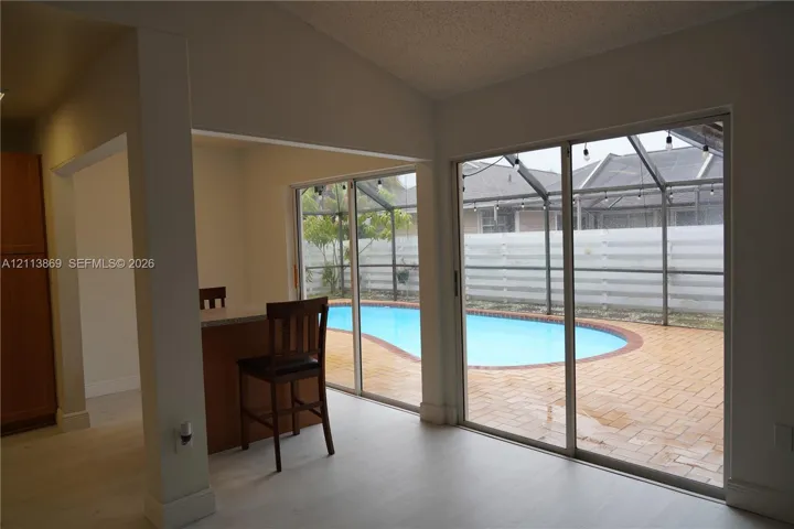 Sliding glass doors opening to a screened-in lanai featuring a swimming pool, brick paver patio, and privacy fencing