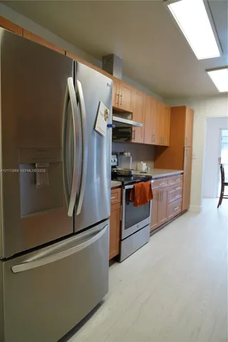 Kitchen featuring wood-finish cabinetry, stainless steel refrigerator, stainless steel range with overhead hood, and light-tone wood-finish flooring