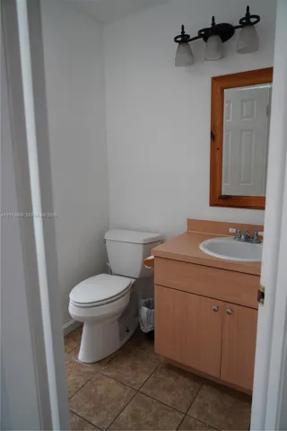 Vanity with wood-finish cabinetry, inset sink, tile flooring, wall-mounted mirror with wood frame, and three-light fixture