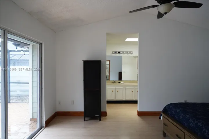 Vaulted ceilings, sliding glass door, light-toned flooring, bathroom vanity with integrated cabinetry, and ceiling fan with light fixture
