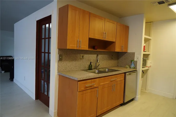 Kitchen featuring wood-finish cabinetry, speckled solid-surface countertops, dual-basin stainless steel sink with pull-down faucet, integrated dishwasher, and a glass-paneled entry door