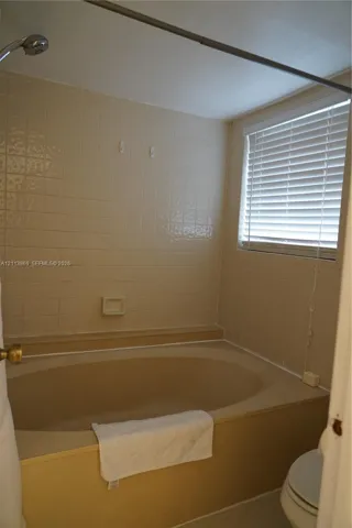 Built-in soaking tub with a tiled surround, integrated soap dish, and a wall-mounted shower head