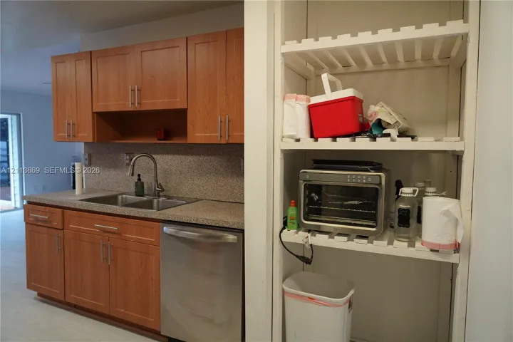 Kitchen featuring wood-finish cabinetry, stone-textured countertops, stainless steel dual-basin sink with arched faucet, stainless steel dishwasher, and built-in slatted shelving