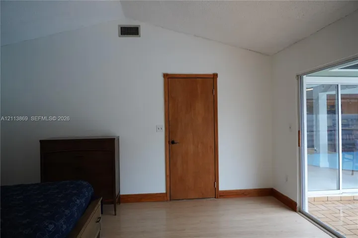 Vaulted ceiling with a wood-finish door, wood-finish door casing, and a sliding glass door providing external access