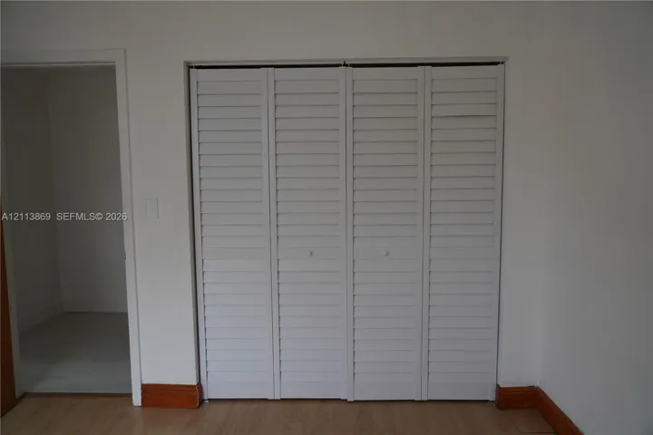 Four-panel white louvered bifold closet doors with circular knobs and wood-finish flooring