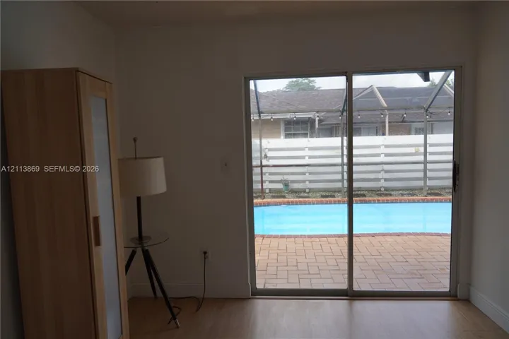 Sliding glass door opening to a brick-paved patio, in-ground swimming pool, and a screen-enclosed pool area with wood-finish flooring