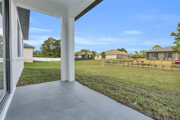Covered concrete patio featuring large-format gray tile flooring, exterior stucco siding, and an expansive lawn area enclosed by a wooden rail fence