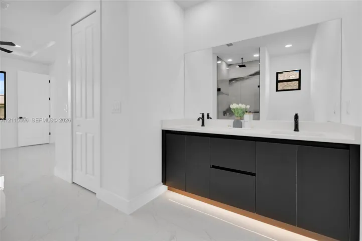 Floating dual-vanity featuring matte black fixtures, solid-surface countertop, under-cabinet lighting, and large wall-to-wall mirror set against stone-finish flooring