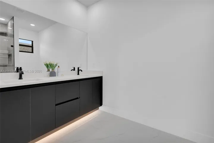 Dual-vanity cabinet with matte black fixtures, quartz countertop, large frameless mirror, integrated under-cabinet lighting, and large-format tile flooring