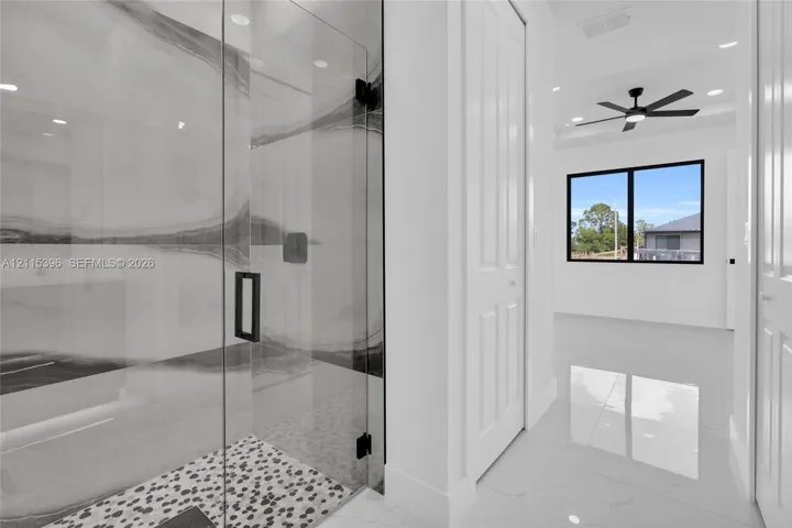 Walk-in shower featuring large-format stone-patterned tile, frameless glass enclosure, pebble-stone flooring, and matte black hardware, complemented by polished tile flooring and recessed lighting