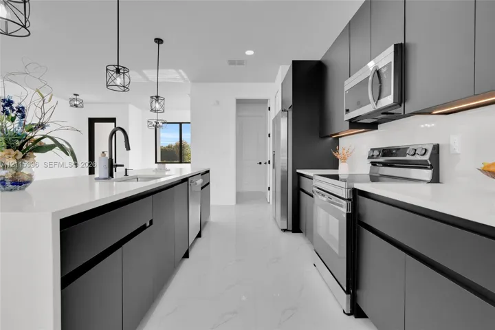 Kitchen featuring flat-panel cabinetry, quartz countertops, stainless steel appliances, large kitchen island with integrated sink, and pendant lighting