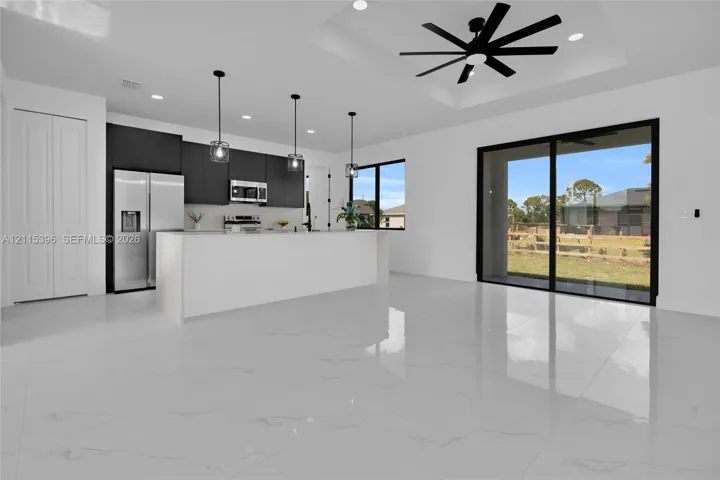 Open-concept kitchen featuring dark flat-panel cabinetry, a central island with a stone-finish countertop, polished tile flooring, a tray ceiling with a matte black ceiling fan, and large sliding glass doors
