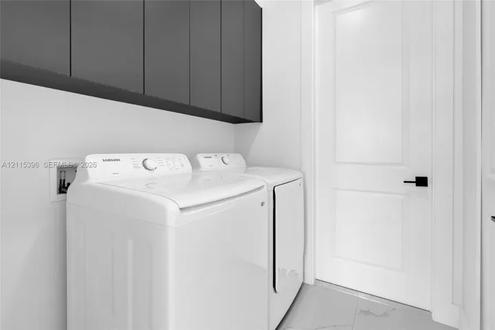 Laundry room featuring charcoal slab-front cabinetry, neutral tile flooring, and a solid-core panel door with matte black hardware