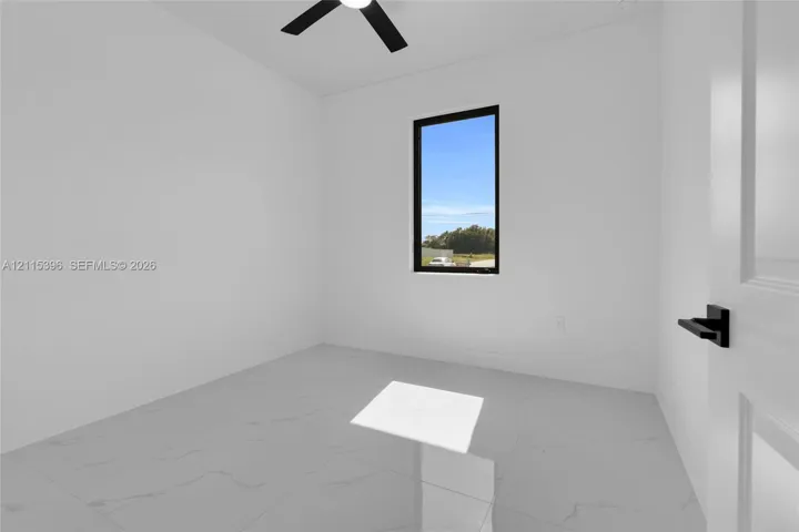 Interior space featuring white stone-finish tile flooring, matte black ceiling fan, black-framed window, and a door with black hardware