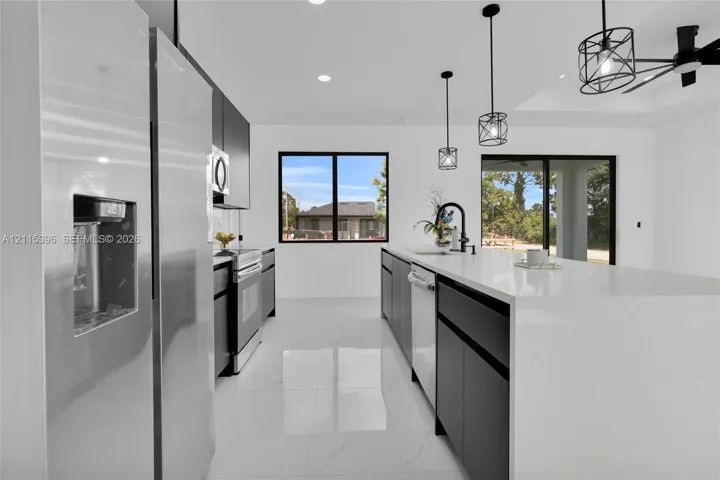 Kitchen featuring dark cabinetry, expansive white stone-surface island, stainless steel appliances, large-format tile flooring, and matte black pendant lighting
