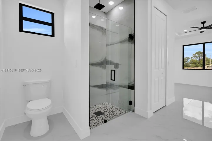 Walk-in shower featuring a glass enclosure, patterned tile flooring, and a rainfall showerhead, complemented by recessed lighting and large-format porcelain tile flooring